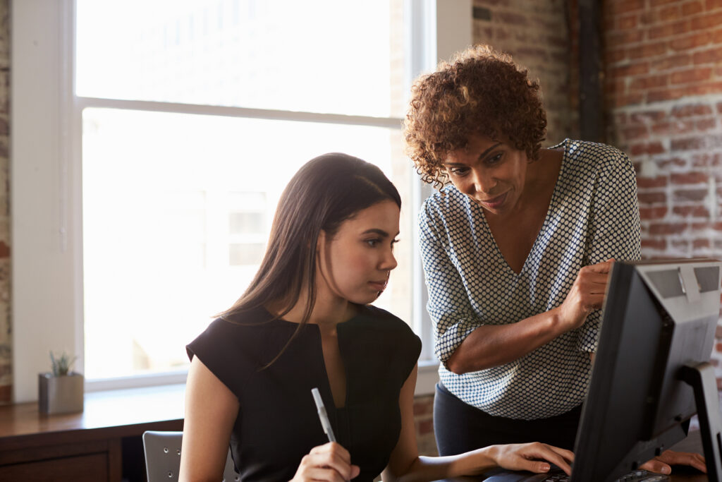 Two female colleagues in a modern office looking intently at a computer screen together, collaborating on a digital marketing strategy for Google and AI search results.