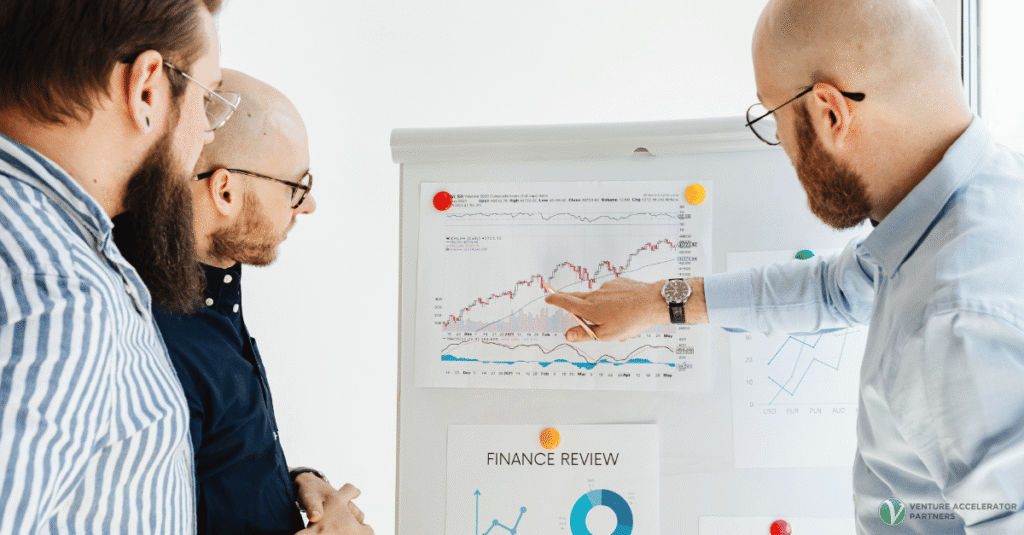Three professionals analyzing financial metrics and line charts on a whiteboard during a discovery phase, highlighting why B2B startups must validate pain and pricing early.